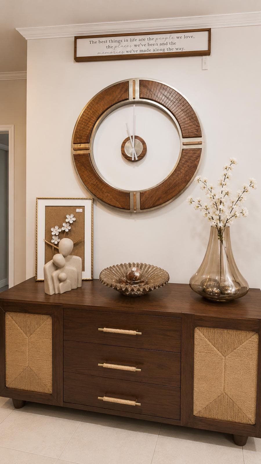 A walnut sideboard with woven panels, styled with a sculpture, a glass vase of blossoms and a wooden wall clock